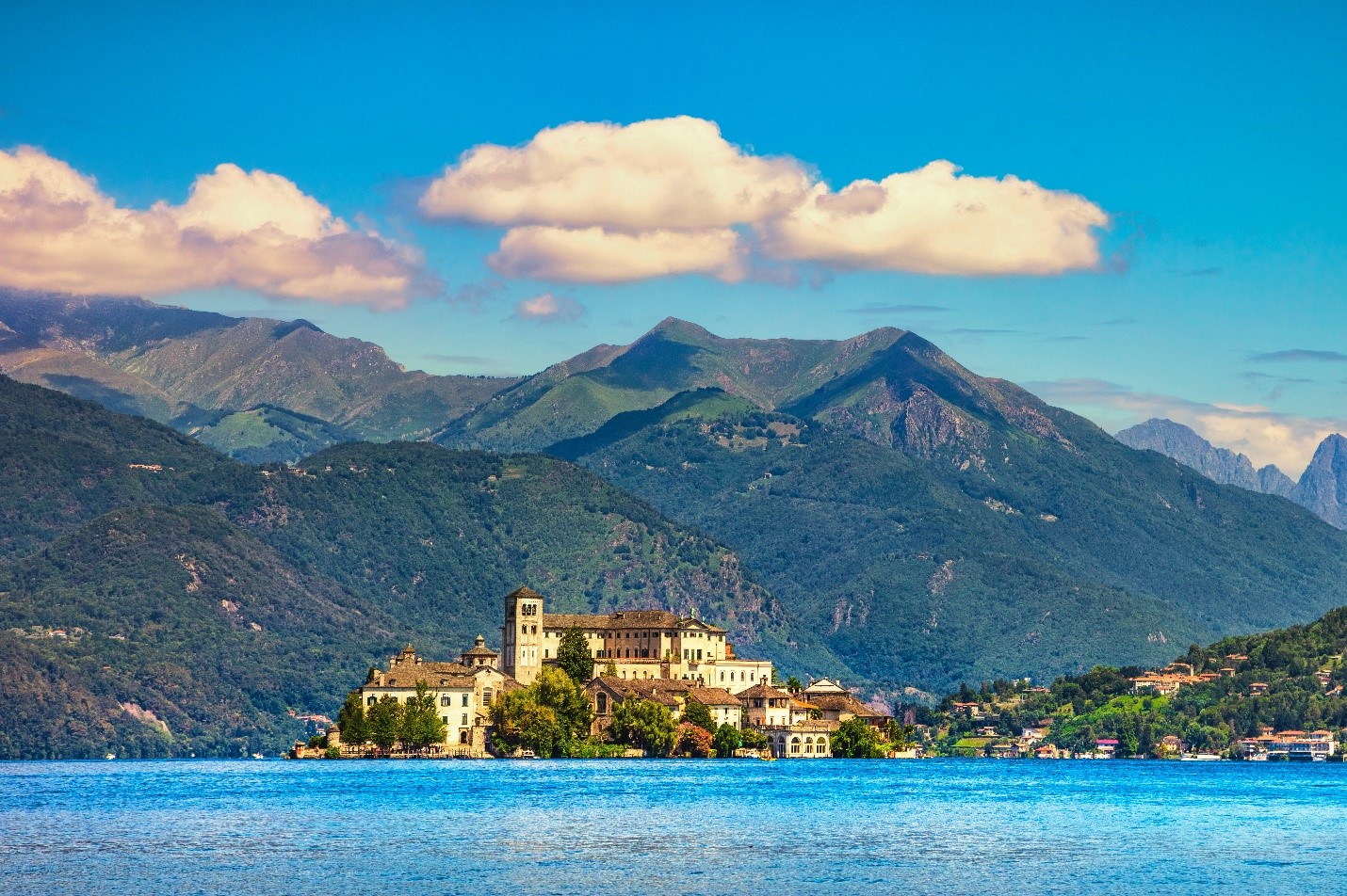 Stone buildings on Lake Orta with towering mountains behind.