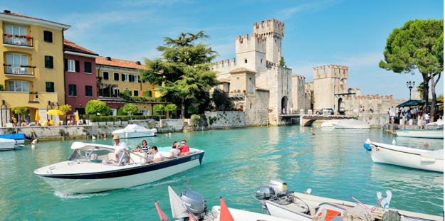 Boats in a harbor with a castle in the background on Lake Garda.