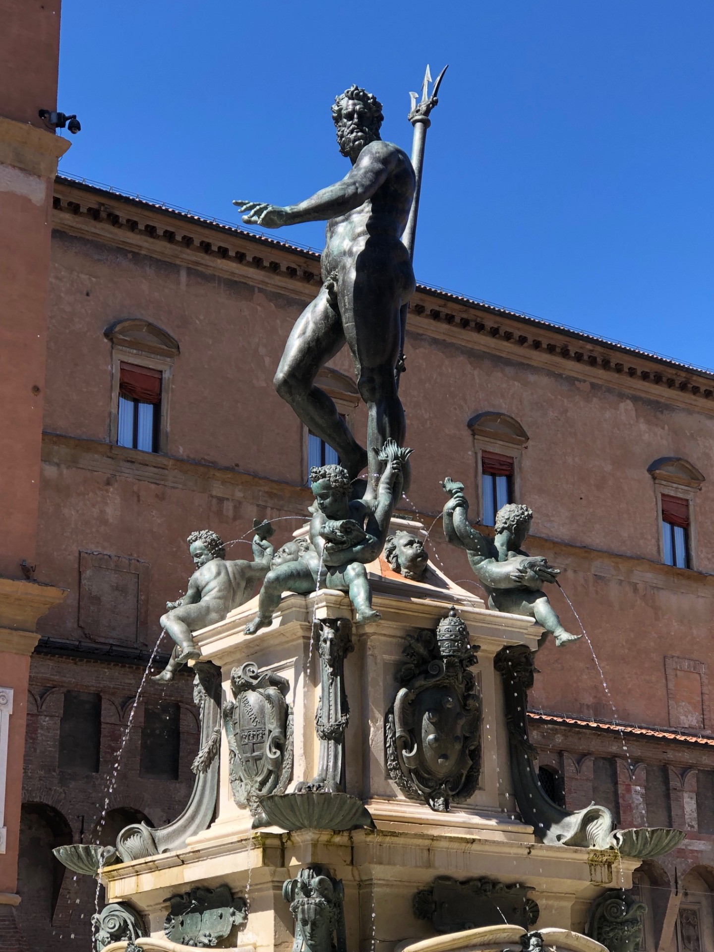 A detailed statue of Neptune stands atop a fountain in Bologna's Piazza Nuttuno, framed by the architecture of a nearby building.